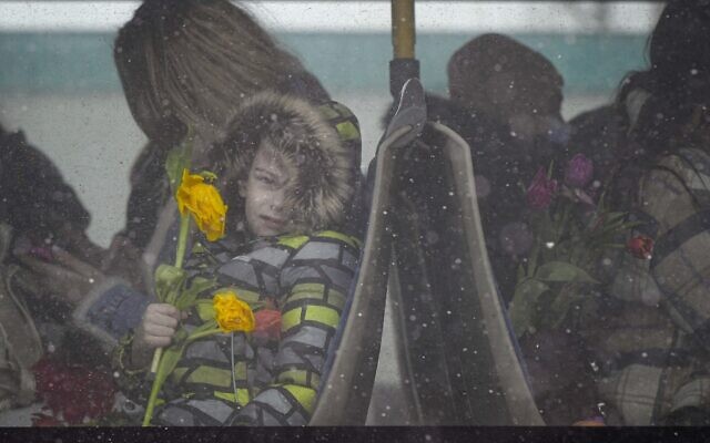 A refugee child fleeing the conflict from neighboring Ukraine holds flowers as he sits on a bus, at the Romanian-Ukrainian border, in Siret, Romania, Tuesday, March 8, 2022.  (AP Photo/Andreea Alexandru)