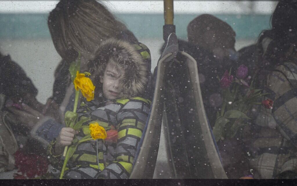 A refugee child fleeing the conflict from neighboring Ukraine holds flowers, given out to celebrate International Women's Day, as he sits on a bus, at the Romanian-Ukrainian border, in Siret, Romania, March 8, 2022 (AP Photo/Andreea Alexandru)