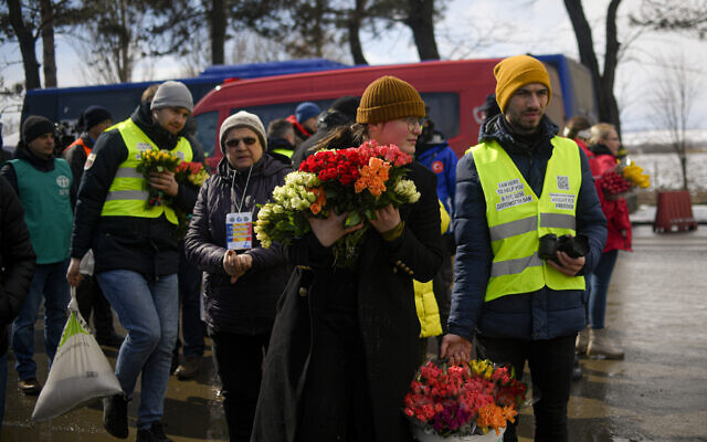 Volunteers hold flowers to give to women fleeing the conflict from neighbouring Ukraine on International Women's Day, at the Romanian-Ukrainian border, in Siret, Romania, March 8, 2022 (AP Photo/Andreea Alexandru)