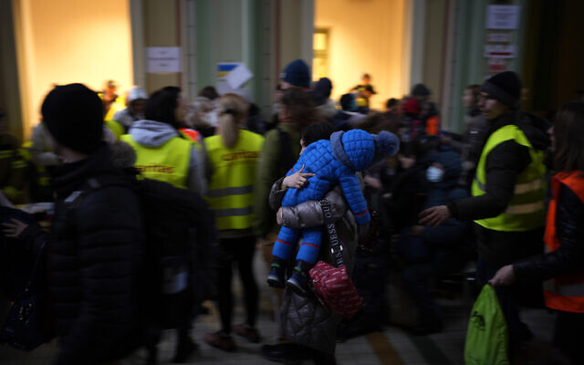 A woman carries a child in a winter suit, after fleeing Ukraine and arriving at the train station in Przemysl, Poland, March 8, 2022 (AP Photo/Daniel Cole)