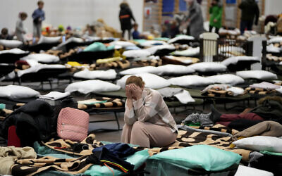 A woman puts her head in her hands as she sits on a cot in a shelter, set up for displaced persons fleeing Ukraine, inside a school gymnasium in Przemysl, Poland, March 8, 2022 (AP Photo/Markus Schreiber)