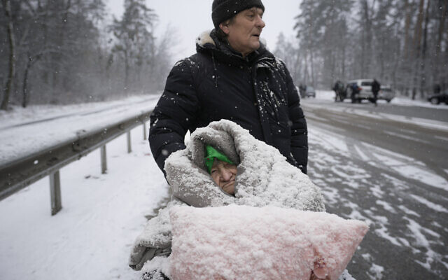 An elderly woman is coated in snow as she sits in a wheelchair after being evacuated from Irpin, on the outskirts of Kyiv, Ukraine, March 8, 2022. (AP Photo/Vadim Ghirda)