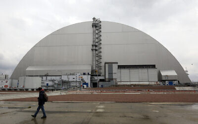 A man walks past a shelter covering the exploded reactor at the Chernobyl nuclear plant, in Chernobyl, Ukraine, on April 15, 2021. (AP Photo/Efrem Lukatsky, File)