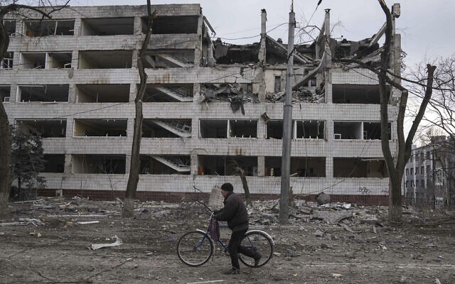 A man walks with a bicycle in front of a damaged by shelling in Mariupol, Ukraine, March 10, 2022. (AP Photo/Evgeniy Maloletka)