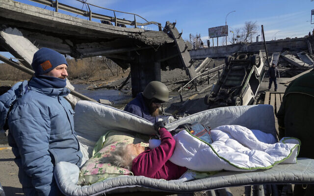 Volunteers pass an improvised path under a destroyed bridge as they evacuate an elderly resident in Irpin, some 25 kilometers (16 miles) northwest of Kyiv, Friday, on March 11, 2022. (AP/Efrem Lukatsky)