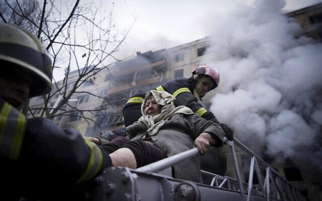 In this photo released by Ukrainian State Emergency Service press service, firefighters evacuate an elderly woman from an apartment building hit by shelling in Kyiv, Ukraine, March 14, 2022. (Ukrainian State Emergency Service via AP)