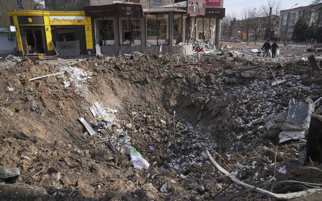 People walk past a crater from the explosion in Mira Avenue (Avenue of Peace) in Mariupol, Ukraine, March 13, 2022. (AP/Evgeniy Maloletka)