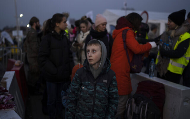 A boy stands with a group of people fleeing Ukraine as they stand in a line after arriving at the border crossing in Medyka, Poland, on Monday, March 14, 2022. (AP Photo/Petros Giannakouris)