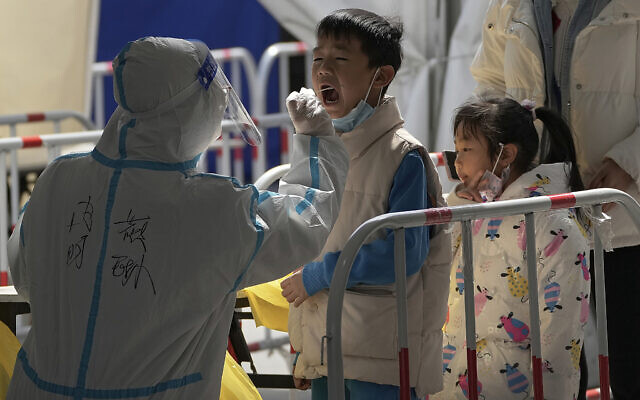 A health worker in protective suit takes a throat swab sample from a child at a coronavirus testing site, March 21, 2022, in Beijing, China (AP Photo/Andy Wong)