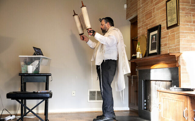 Wrapped in tefillin, Rabbi Haim Ovadia holds a Torah scroll up toward an electronic tablet so that the 32 people attending his Zoom meeting can see it during a virtual morning minyan transmitted from Ovadia's home in Potomac MD, on April 6, 2020. (AP Photo/Jacquelyn Martin, File)
