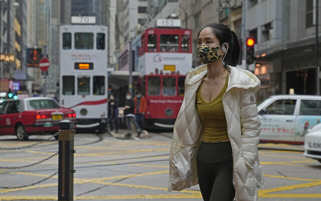 A woman wearing a mask walks across a street in Hong Kong, March 25, 2022. (AP Photo/Kin Cheung)