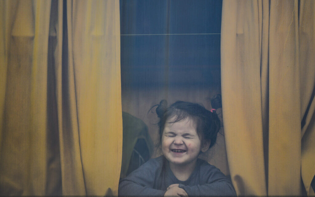 A child refugee fleeing the war from neighbouring Ukraine with her family grimaces as she sits in a bus after crossing the border by ferry at the Isaccea-Orlivka border crossing, in Romania, March 25, 2022. (AP Photo/Andreea Alexandru)