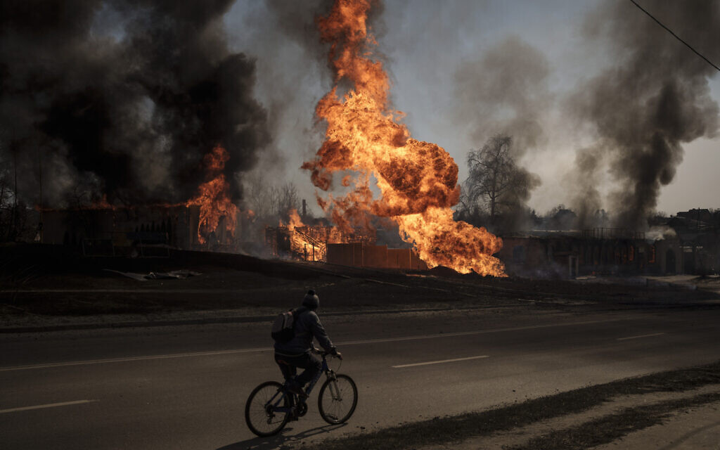 A man rides his bike past flames and smoke rising from a fire following a Russian attack in Kharkiv, Ukraine, March 25, 2022. (AP Photo/Felipe Dana)