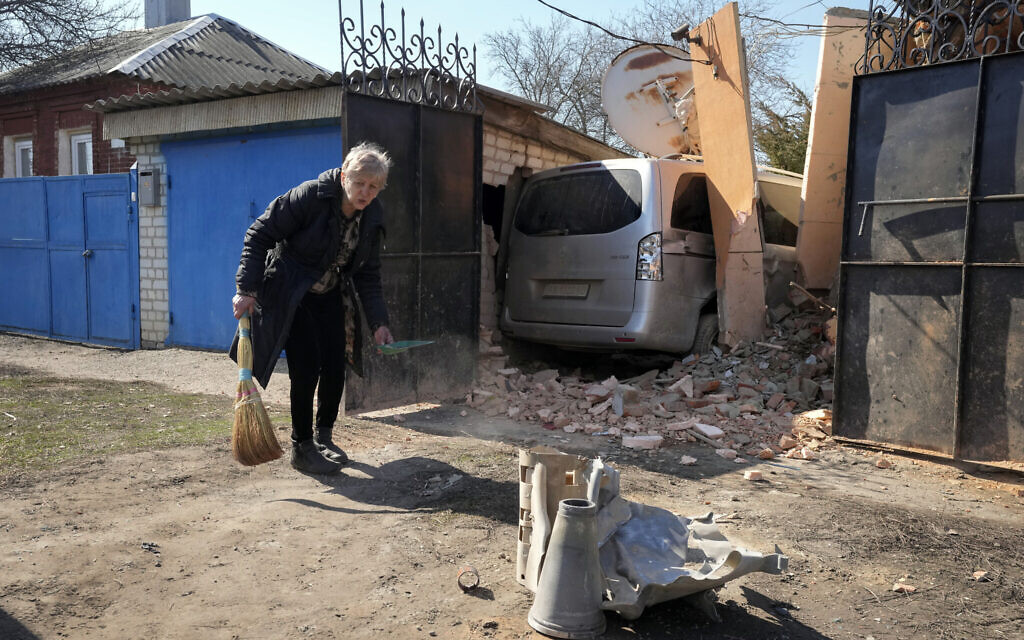 A woman sweeps in front of her house, fragments of a Russian rocket in the foreground, following a Russian attack in Kharkiv, Ukraine, March 25, 2022. (AP Photo/Efrem Lukatsky)