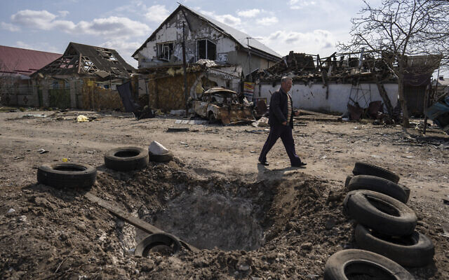 A man walks behind a crater created by a bomb and in front of damaged houses following a Russian bombing earlier this week, outskirts Mykolaiv, Ukraine, Friday, 25, 2022.(AP Photo/Petros Giannakouris)