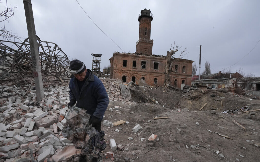 A man holds fragments of a rocket launched by the Russian forces at night, a rocket crater behind him, in the center of Kharkiv, Ukraine, March 27, 2022. (AP Photo/Efrem Lukatsky)