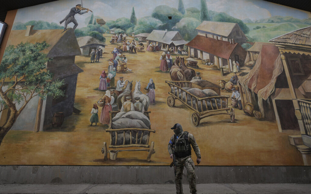 A member of the security team walks by a Fidler on the Roof themed mural at the Anatevka Jewish settlement outside Kyiv, Ukraine, March 27, 2022. (AP Photo/Vadim Ghirda)