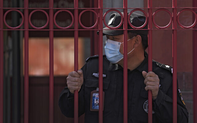 A security guard wearing a mask to help protect from the coronavirus stands behind a fence, Monday, March 28, 2022, in Beijing. China began its largest lockdown in two years Monday to conduct mass testing and control a growing outbreak in its largest city of Shanghai as questions are raised about the economic toll of the nation's "zero-COVID" strategy. (AP Photo/Andy Wong)