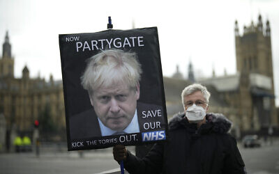An anti-Conservative Party protester holds a placard with an image of British Prime Minister Boris Johnson including the words 'Now Partygate' backdropped by the Houses of Parliament, in London, Dec. 8, 2021. Matt Dunham/AP)