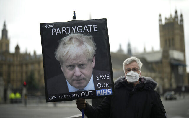 An anti-Conservative Party protester holds a placard with an image of British Prime Minister Boris Johnson including the words 'Now Partygate' backdropped by the Houses of Parliament, in London, Dec. 8, 2021. (Matt Dunham/AP)
