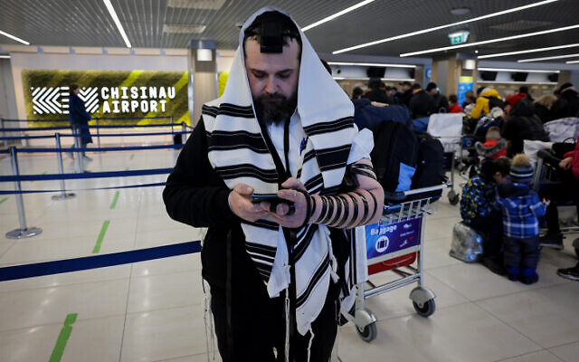A Jewish Ukrainian man who fled Ukraine prays while covered in a prayer shawl at the Chisinau International Airport in Moldova, as he makes his way to Israel, March 6, 2022. (Nati Shohat/Flash90)