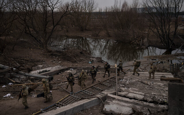Ukrainian soldiers cross an improvised path under a destroyed bridge in Irpin, one outskirts of Kyiv, Ukraine, March 12, 2022. (AP/Felipe Dana)