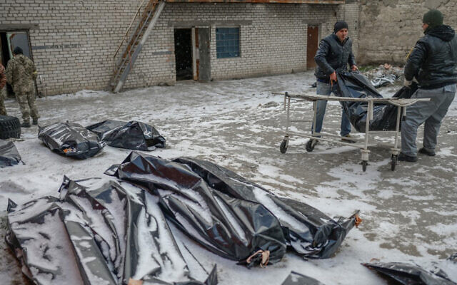 Two men carry a corpse in a body bag to lay it next to others in a snow covered yard in Mykolaiv, a city on the shores of the Black Sea that has been under Russian attack for days on March 11, 2022. (Bulent Kilic/AFP)