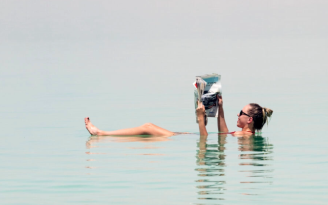 A tourist poses for a picture while floating in the Dead Sea, on June 17, 2018. (Ronen Tivony/NurPhoto/Getty Images via JTA)
