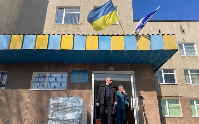 Members of the Israeli field hospital team emerge from the Ukrainian elementary school, whose grounds house the facility, Mostyska, Ukraine, on March 19, 2022. Ukrainian and Israeli flags fly above. (Carrie Keller-Lynn/The Times of Israel)