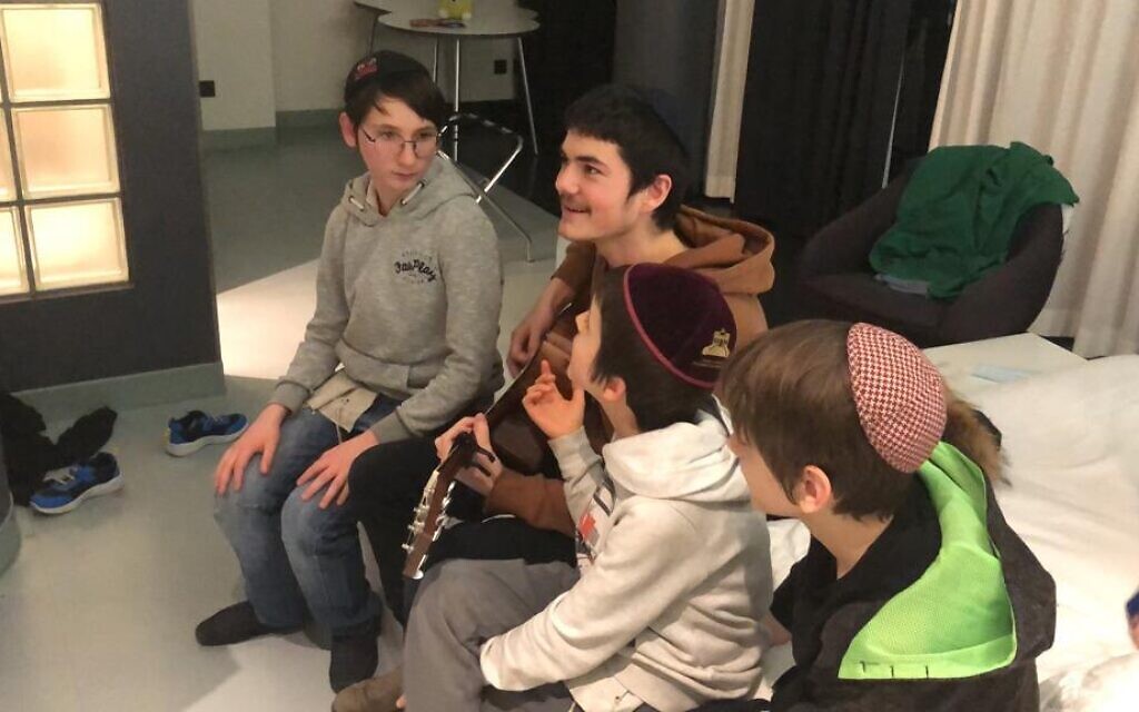 A Chabad Camp Yeka counselor plays guitar with his campers, Jewish orphans from Odessa, after they escaped from Ukraine to Berlin, March 2022 (courtesy Camp Yeka)
