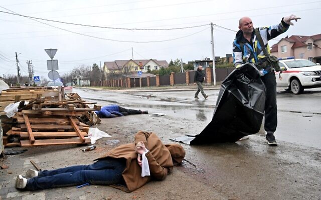 A body of a civilian man with hands tied behind his back lies in the street as a communal worker prepares a plastic body bag to carry him to a waiting car in town of Bucha, not far from the Ukrainian capital of Kyiv on April 3, 2022. (Sergei SUPINSKY / AFP)