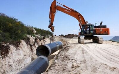 Illustrative: A bulldozer carries a new pipeline by Israel's national water company near Kibbutz Ravid, west of Sea of Galilee on March 16, 2022.(Menahem Kahana/AFP)