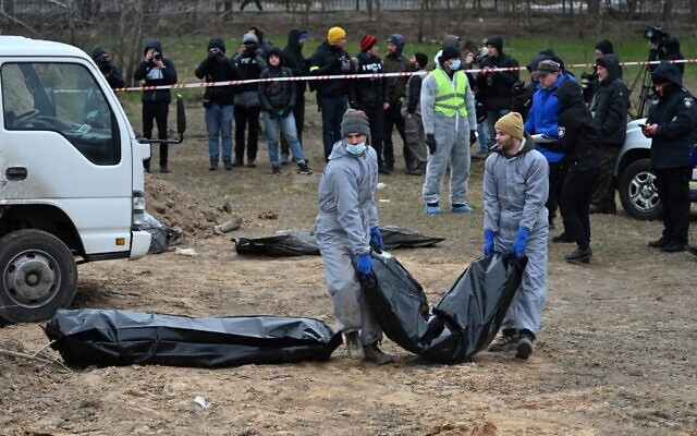 Journalists gather as bodies are exhumed and removed from a mass-grave in the grounds of the St. Andrew and Pyervozvannoho All Saints church in the Ukrainian town of Bucha, northwest of Kyiv on April 13, 2022. (Sergei SUPINSKY / AFP)