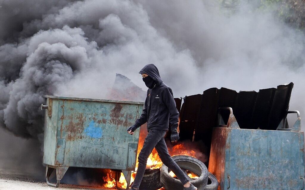 A Palestinian protester walks past burning tires and trash bins, set up as roadblocks in the West Bank village of Burqa during clashes with Israeli forces following a protest against a march by Israelis to the wildcat settlement outpost of Homesh, on April 19, 2022. (JAAFAR ASHTIYEH / AFP)