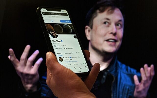 In this photo illustration, a phone screen displays the Twitter account of Elon Musk with a photo of him shown in the background, on April 14, 2022, in Washington, DC. (Olivier DOULIERY / AFP)