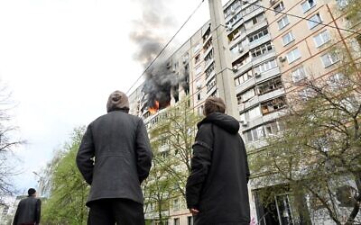 People watch flames coming out of an appartement in a residential building of the northern outskirts of Kharkiv following shelling, on April 22, 2022. (Sergey Bobok/AFP)