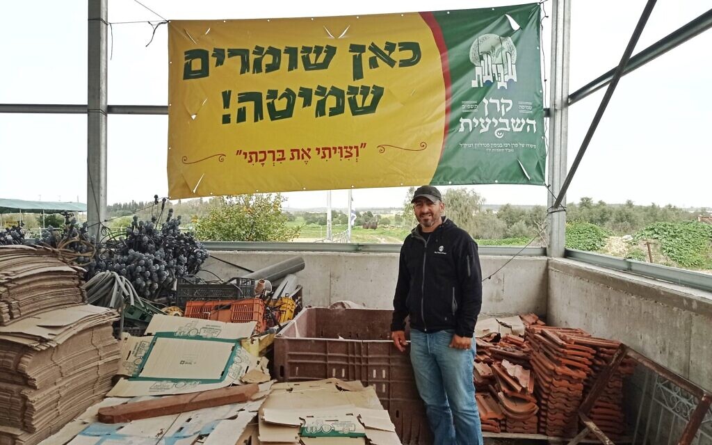 Doron Toweg stands below a sign provided by Keren Hashviis, a group that supports Jewish farmers in Israel who obey shmita laws. (Deborah Danan/JTA)