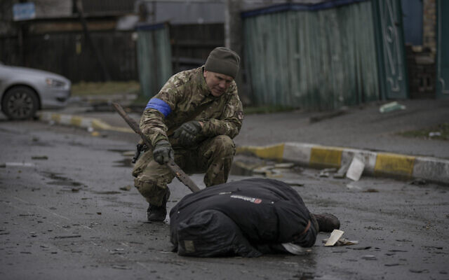 A Ukrainian serviceman checks the dead body of a civilian for booby traps in the formerly Russian-occupied Kyiv suburb of Bucha, Ukraine, April 2, 2022. (AP Photo/Vadim Ghirda)