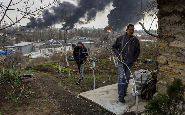 Men walk in a yard as smoke rises in the air in the background after shelling in Odessa, Ukraine, April 3, 2022. (AP Photo/Petros Giannakouris)