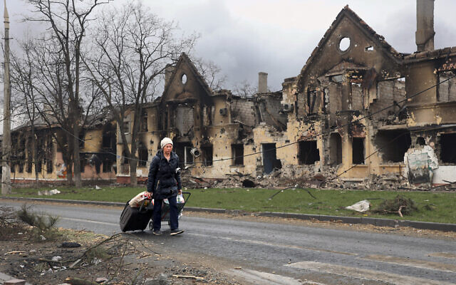 A woman pulls her bags past houses damaged during a fighting in Mariupol, on the territory which is now under the Government of the Donetsk People's Republic control, eastern in Mariupol, Ukraine, on April 8, 2022. (AP Photo/Alexei Alexandrov)