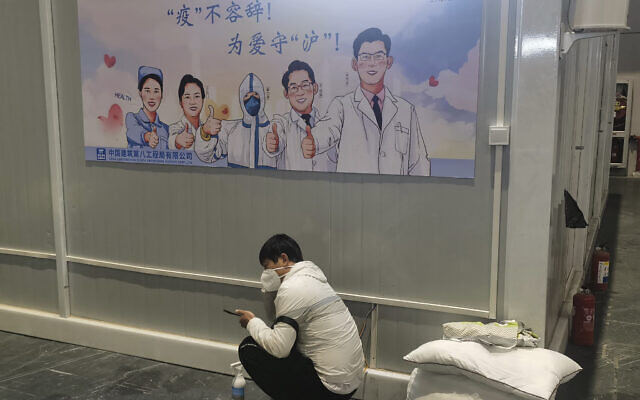 A resident staying at a temporary hospital converted from the National Exhibition and Convention Center to quarantine COVID-positive people squats near a propaganda poster calling for action against the pandemic in Shanghai, China on April 18, 2022.(Chinatopix via AP)