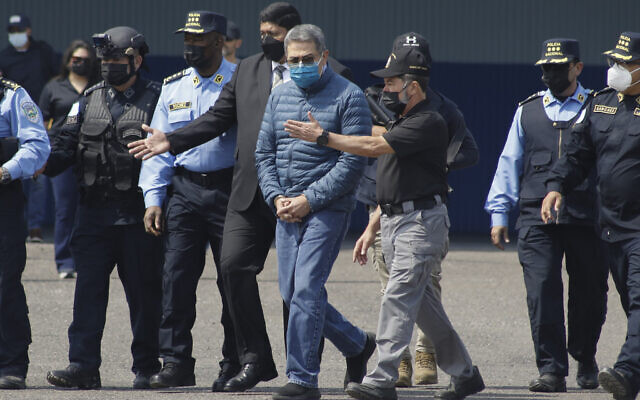 Former Honduran President Juan Orlando Hernandez, center, is taken in handcuffs to a waiting aircraft as he is extradited to the United States, at an Air Force base in Tegucigalpa, Honduras, Thursday, April 21, 2022. (AP Photo/Elmer Martinez)
