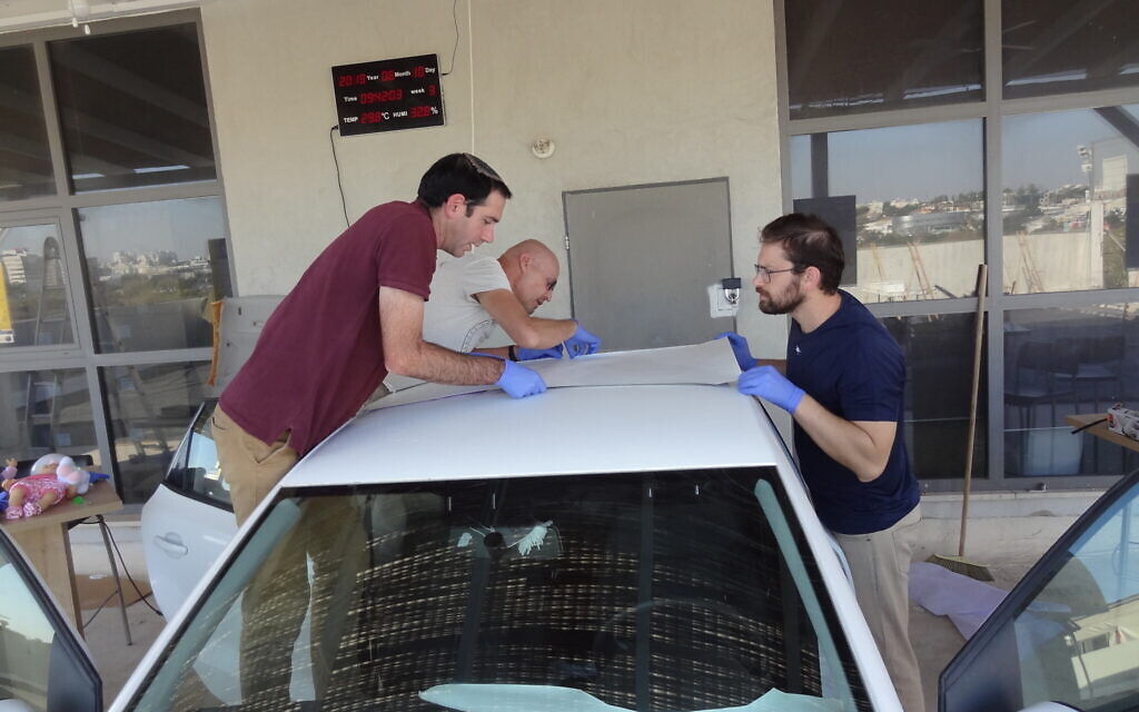 SolCold team members apply the company's cool-by-sunlight film onto the rooftop of a vehicle at the startup's testing site in Ness Ziona. (Courtesy)