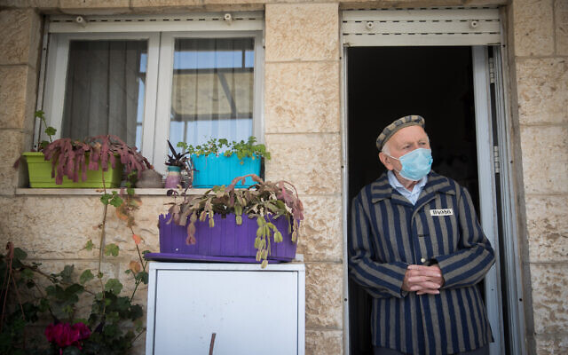 Illustrative: Joseph Kleinman, a 90-year-old Holocaust survivor who survived Auschwitz and Dachau Nazi death camp wearing a face mask as he stands at his porch in Jerusalem, during the Holocaust Remembrance Day, April 21, 2020. (Yonatan Sindel/Flash90)