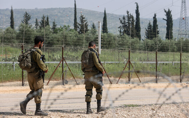 File: Israeli soldiers stand guard near a hole in the security fence, as Palestinians try to cross into Israel, near Mevo Horon, April 10, 2022. (Flash90)