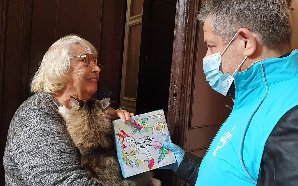 Svetlana Niselevitch receives a haggadah for Passover from a JDC staff member outside her home in Odesa, Ukraine, April 8, 2022. (JDC via JTA)