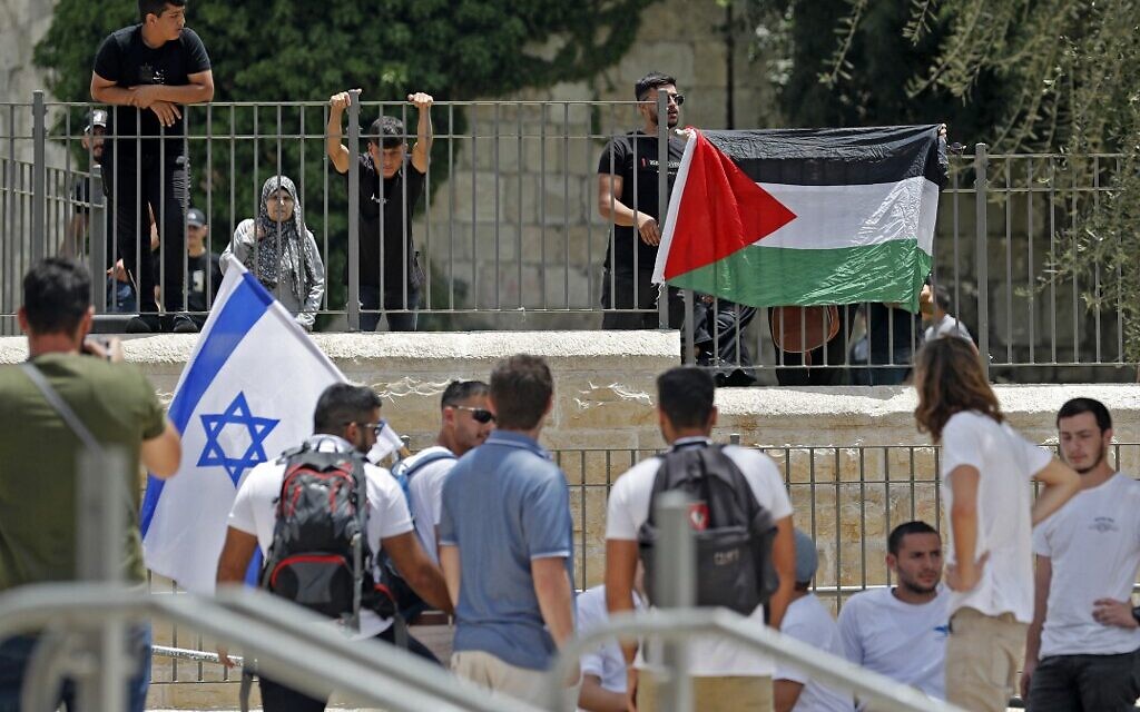 Palestinians lift their national flag on a fence across from Israelis lifting theirs at the Damascus Gate to the Old City of Jerusalem, as Israelis mark Jerusalem Day, on May 29, 2022. (Ahmad GHARABLI / AFP)