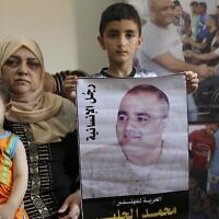 Amal el-Halabi (left) holds her grandson Fares while her grandson Amro, 7 (center) holds a picture of his father Mohammed el-Halabi, at their family home in Gaza city. The Arabic on the picture reads, " the man of humanity." August 8, 2016. (AP Photo/Adel Hana, File)