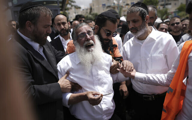 Mourners comfort a man overcome with grief at the funeral processions for Yonatan Havakuk and Boaz Gol, a day after they were killed in a stabbing attack in the central Israeli city of Elad, May 6, 2022. (AP Photo/Ariel Schalit)