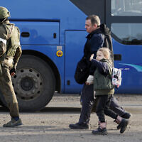 A man and a girl who left a shelter in the Metallurgical Combine Azovstal walk to a bus escorted by Russian Army serviceman in Mariupol, eastern Ukraine, on Friday, May 6, 2022. (AP Photo/Alexei Alexandrov)